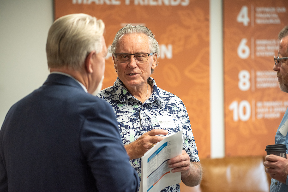Two older men talk to each other over coffee.