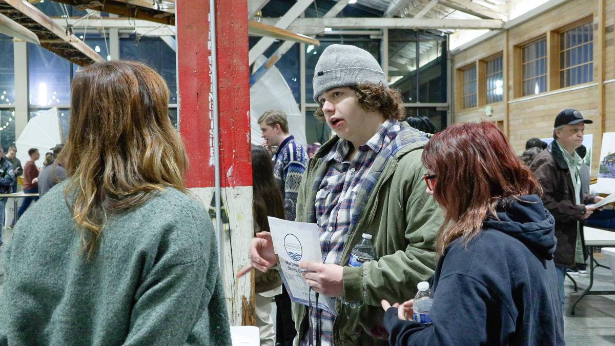 A young man speaks to two women while holding a flyer.